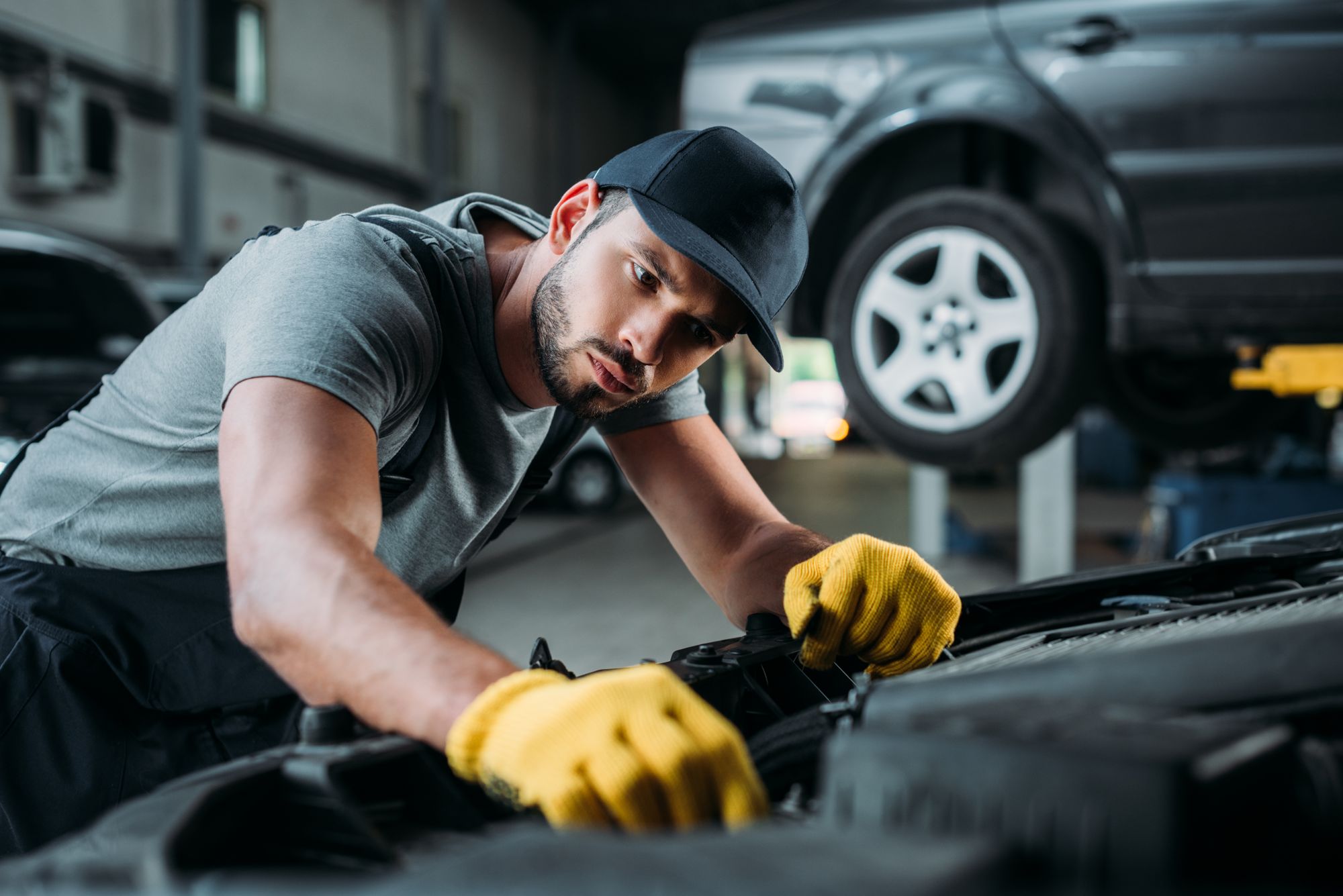 Automechanik v žltých rukaviciach kontroluje motor auta v servise